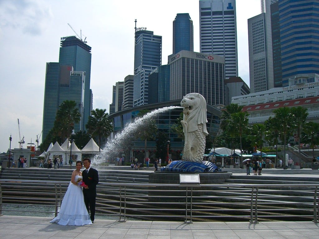 A bride and groom pose in front of Singapore's Merlion
