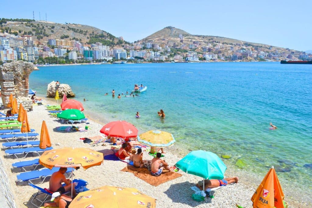 Beachgoers relax on a white pebbled beach under colorful umbrellas in Sarande Albania